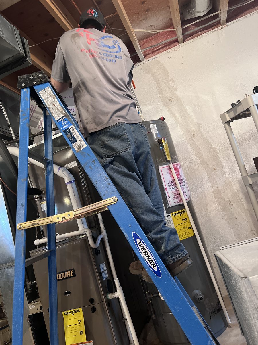 RC Heating & Cooling technician servicing a water heater from a ladder